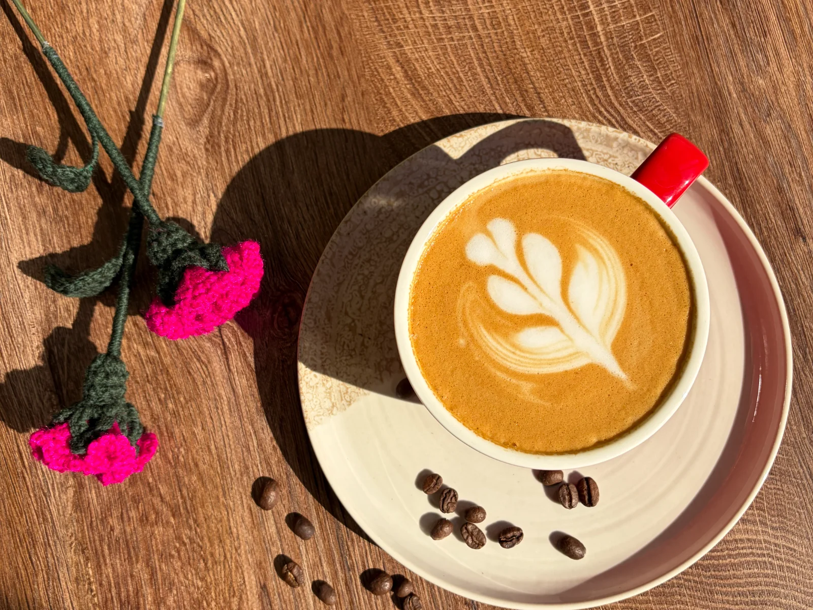 Rose latte art in a red cup beside dried roses at Bloom Bliss Café